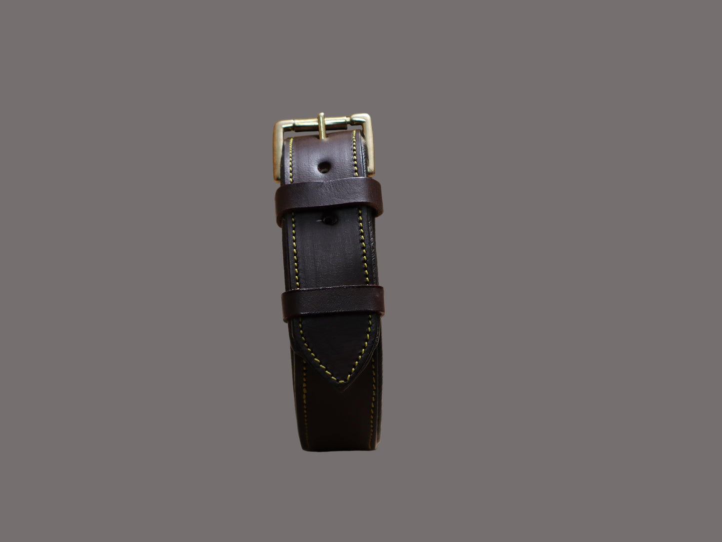 Brown leather strap with gold buckle on a beige surface