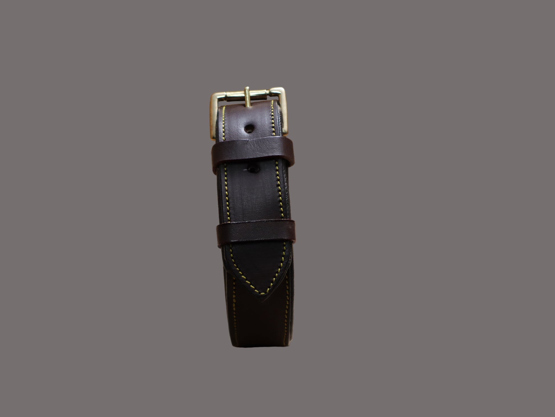 Brown leather strap with gold buckle on a beige surface